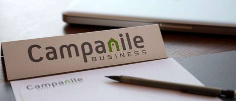 A business card for Campanile Business on a desk with a laptop and a pen.