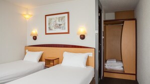 Une chambre d’hôtel avec deux lits, une tête de lit en bois, des lampes fixées au mur et un tableau encadré.