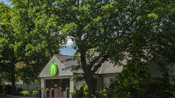 Een gebouw met een groen logo, omgeven door bomen en begroeiing.