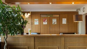 Un comptoir d’accueil avec des meubles de rangement en bois, une plante en pot et divers affiches d’information.