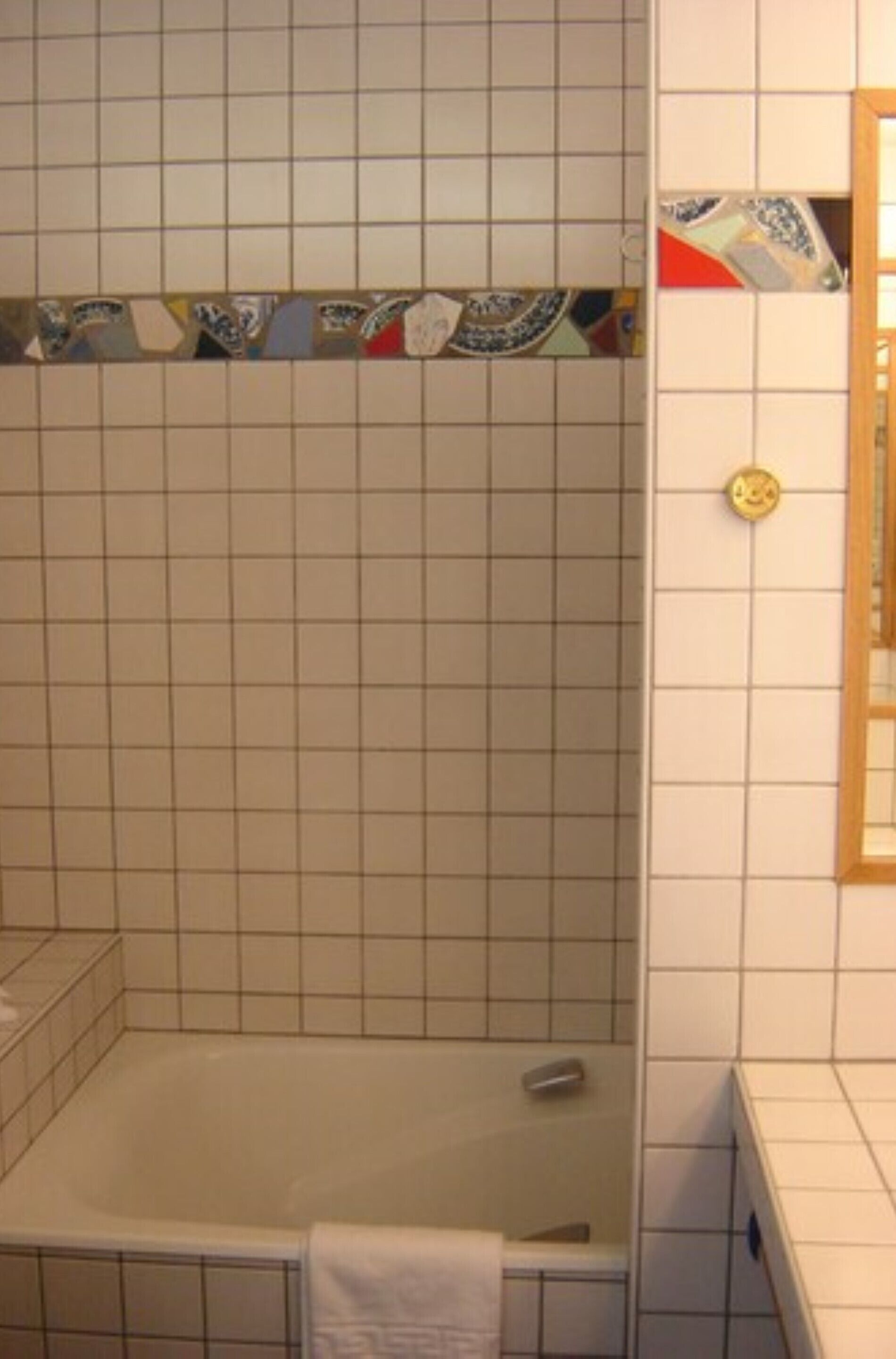 Un bagno con una vasca, pareti piastrellate e una fascia decorativa in ceramica.