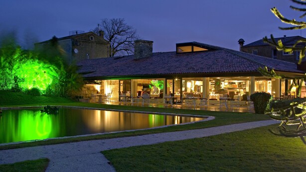 A well-lit outdoor area with a pool, seating, and a building with a tiled roof.