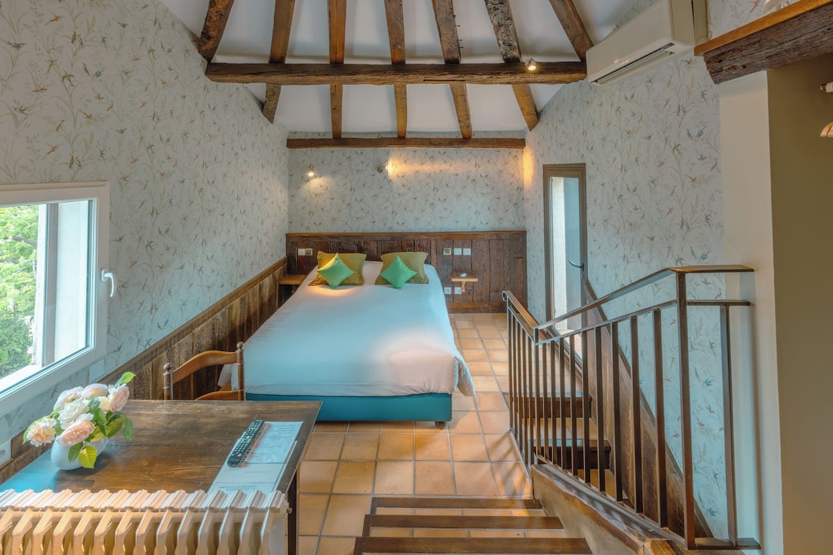 Ein Schlafzimmer mit einem großen Bett, einem Holztisch mit Blumenvase, einem Fenster und einer Treppe.