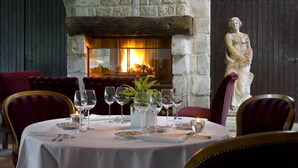 A dining table set for six with wine glasses, plates, and a centerpiece. A stone fireplace with a fire is visible behind the table.