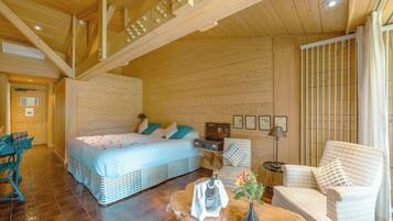 A wooden cabin interior with a bed, a chair, a table, and a desk.