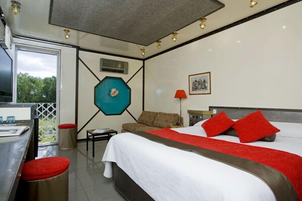 A modern hotel room with a large bed, a sofa, a desk, and a view of the outdoors.