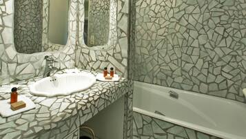 Un baño con pared de mosaicos, un lavamanos blanco, dos espejos y una bañera.