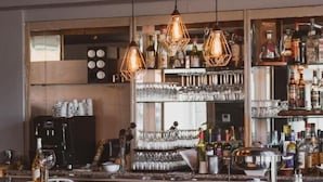 Eine Bar mit Holztresen, hängenden Lampen und einer Auswahl an Flaschen und Gläsern.