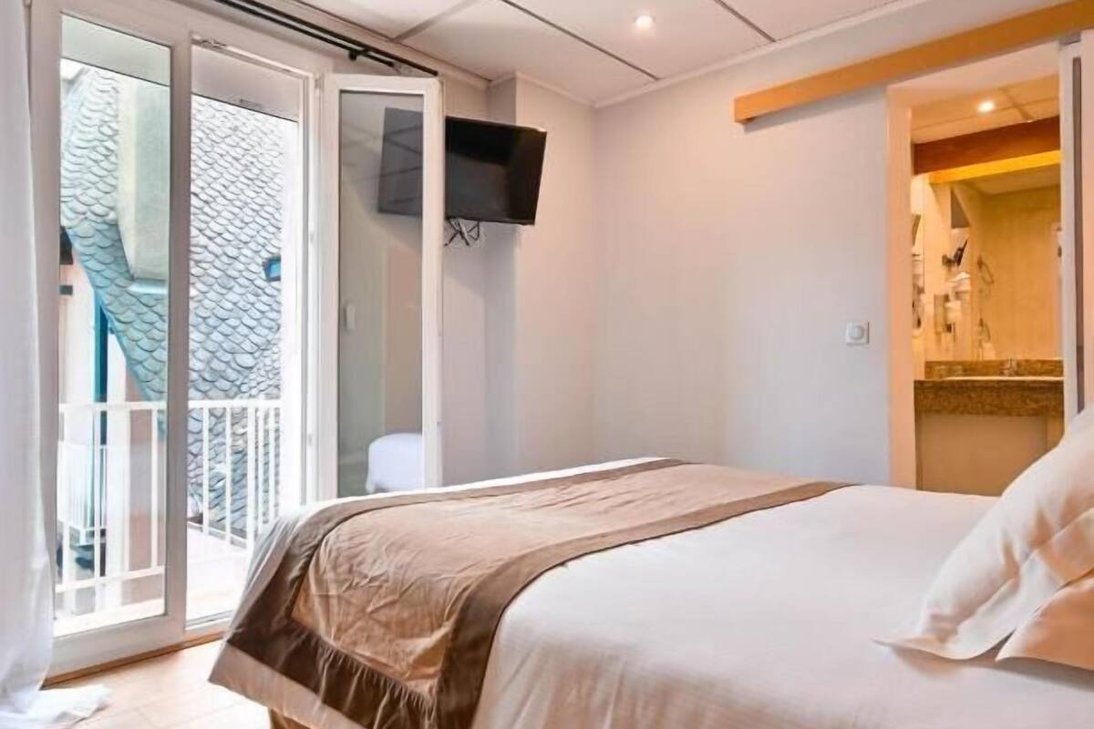 A bedroom with a bed, a television, a sliding glass door, and a bathroom visible through an open door.