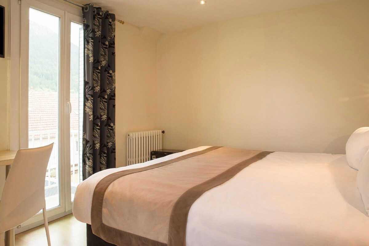 Una habitación de hotel con una cama, una silla, un radiador y una ventana con cortinas.