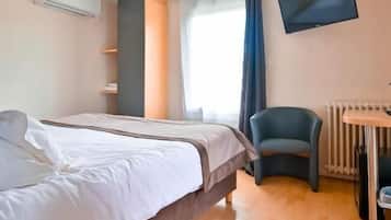 Ein Hotelzimmer mit Bett, Schreibtisch, Stuhl, Fernseher und einem Fenster mit Vorhängen.