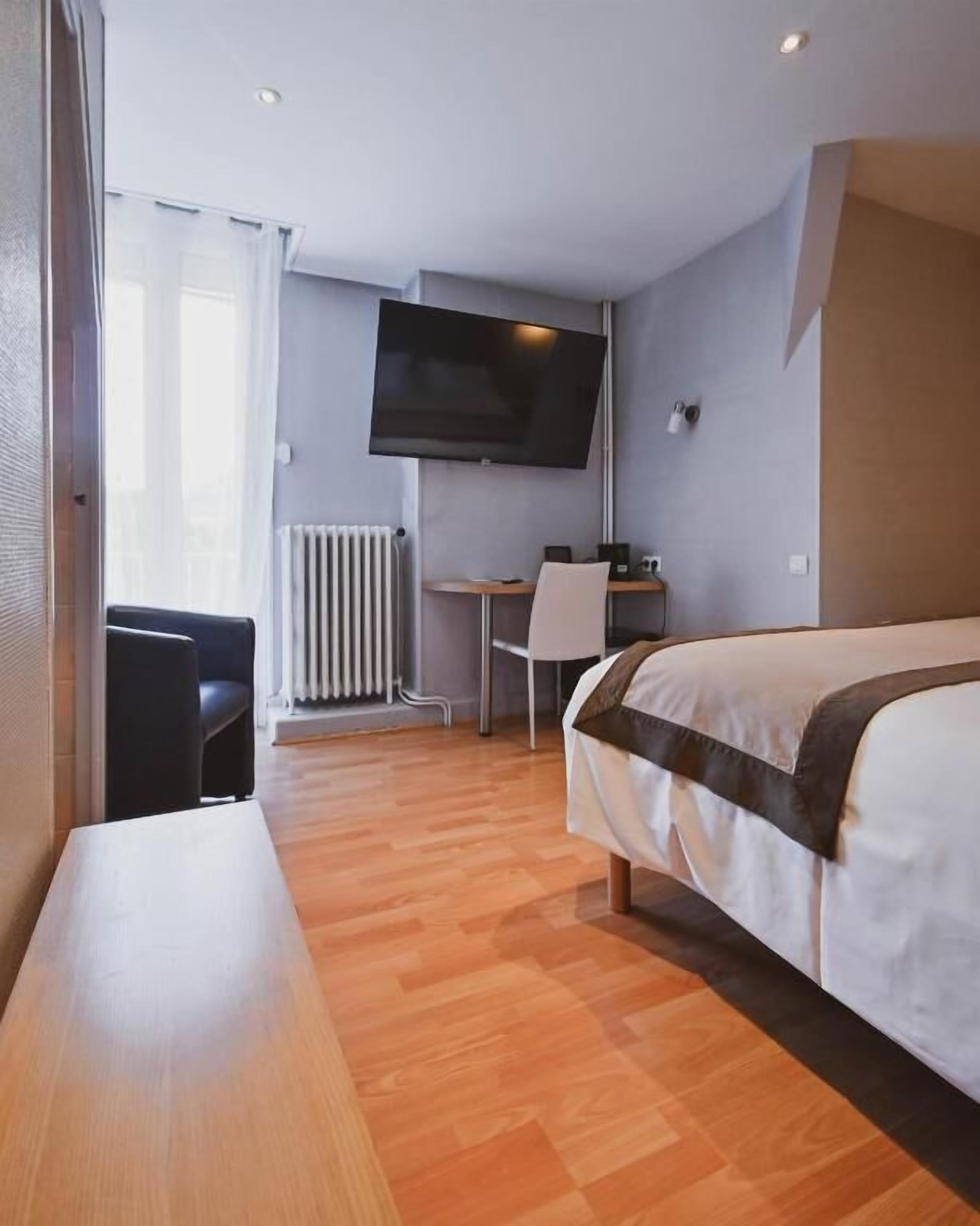 Een hotelkamer met een bed, een bureau, een stoel, een televisie en een radiator.