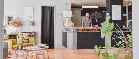 Un vestíbulo de hotel con mostrador de recepción, zona de estar y una planta grande.