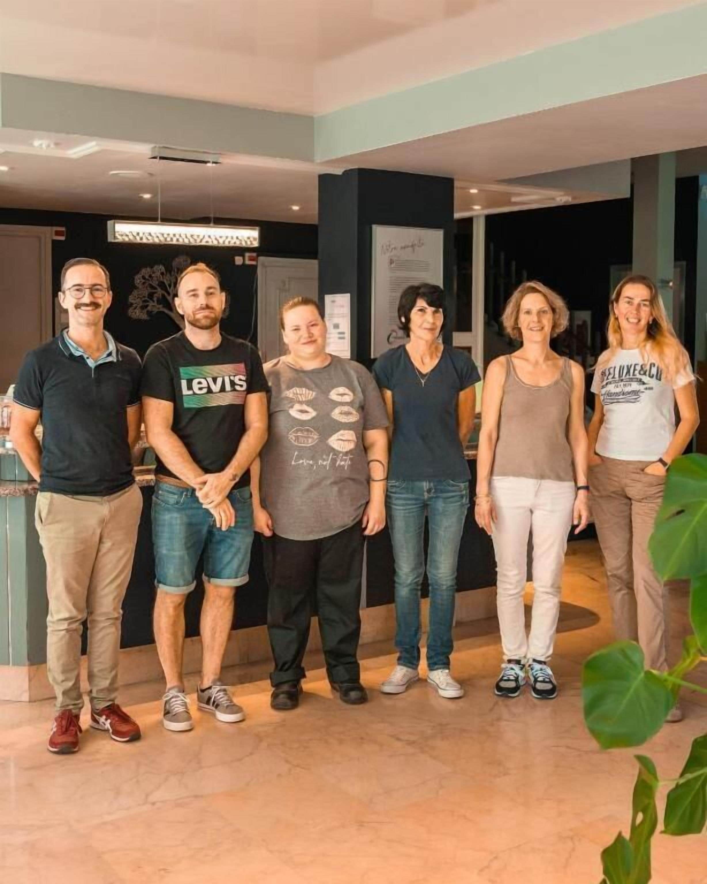 A group of people standing indoors with a modern interior design, including a visible ceiling and wall-mounted signage.