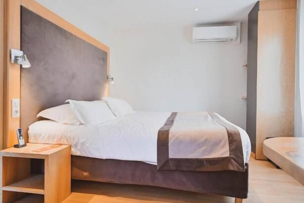 A modern bedroom with a bed, bedside table, and an air conditioning unit.