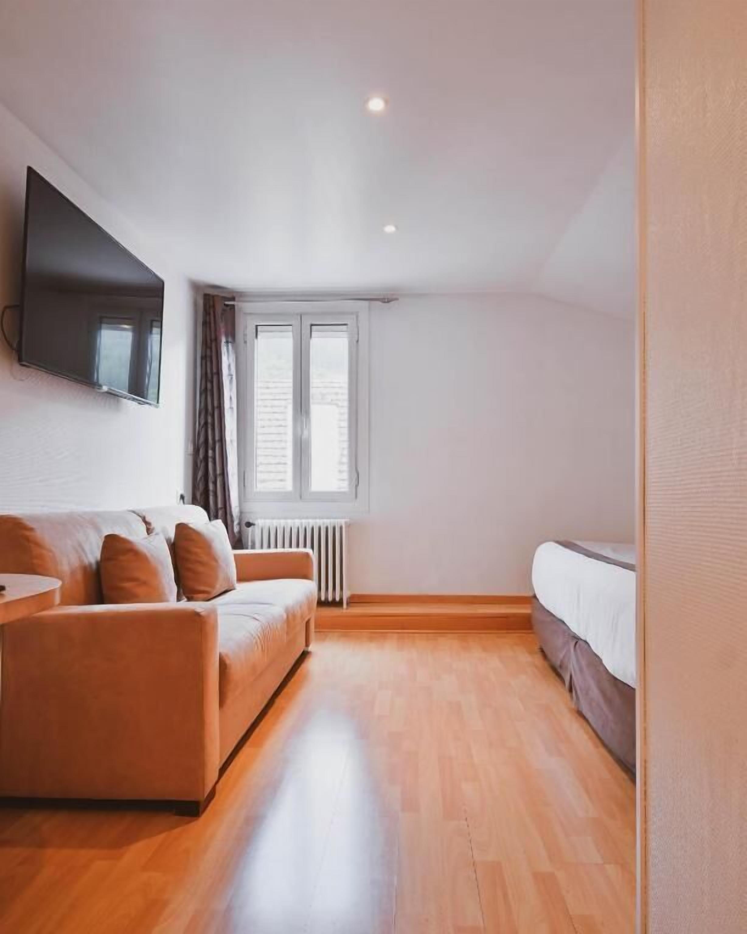 Ein modernes Zimmer mit einer Schlafcouch, einem Bett, einem an der Wand montierten Fernseher und einem Fenster mit Vorhängen.