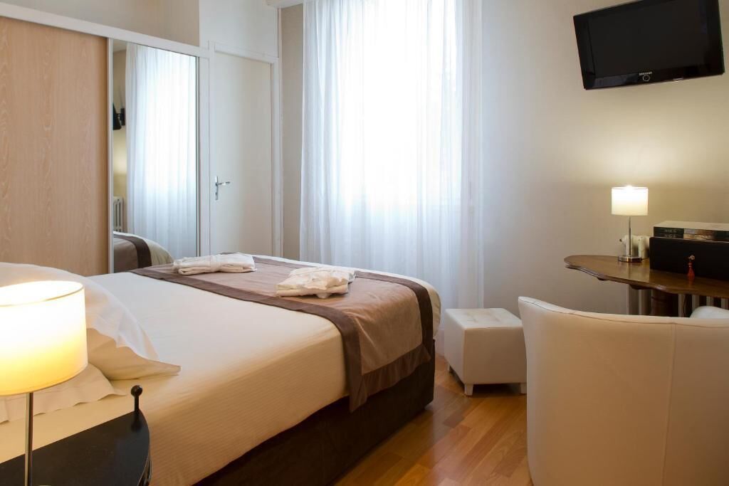 A hotel room with a bed, a desk, a chair, a TV, and a window with curtains.
