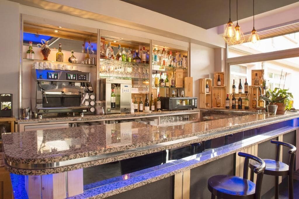 Una zona de bar con encimera de granito, taburetes, una estantería para vinos y una cafetera.