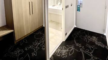 Una habitación de hotel con un armario, un baño con espejo y una alfombra estampada con motivos florales.