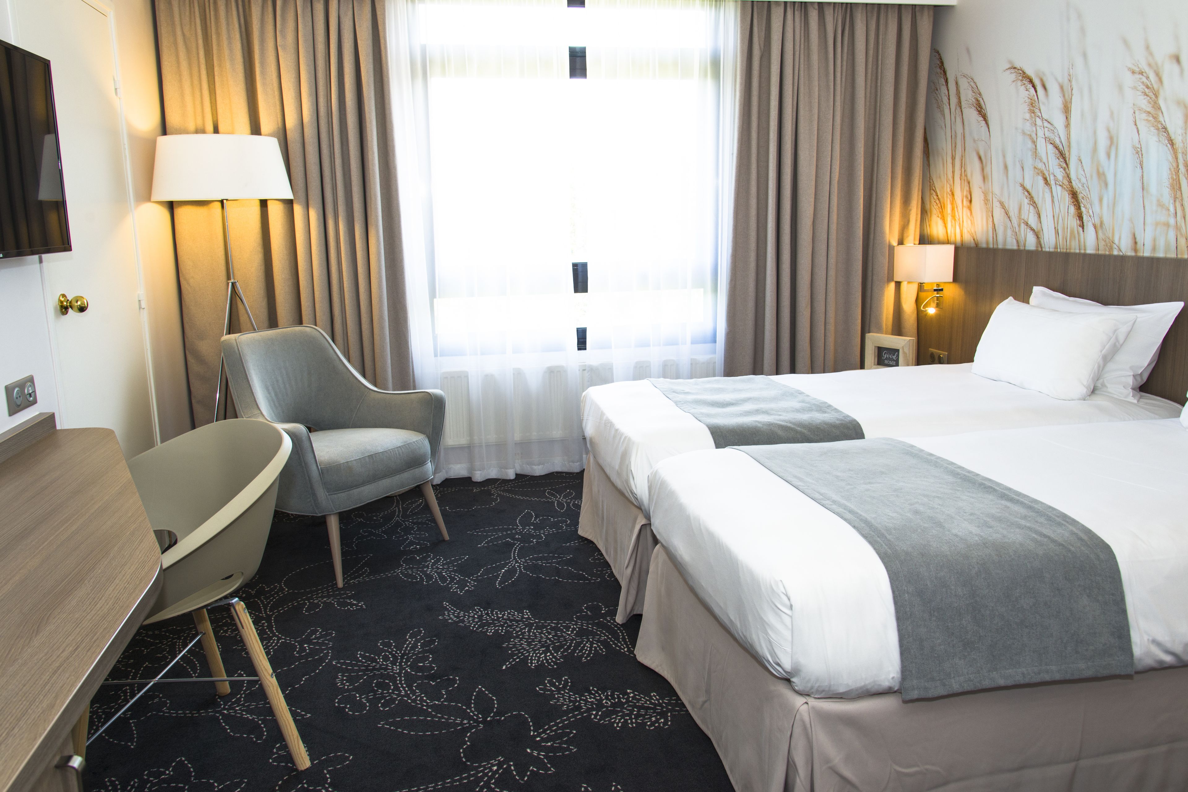 A hotel room with a bed, two bedside tables, a chair, a desk, and a large window with curtains.