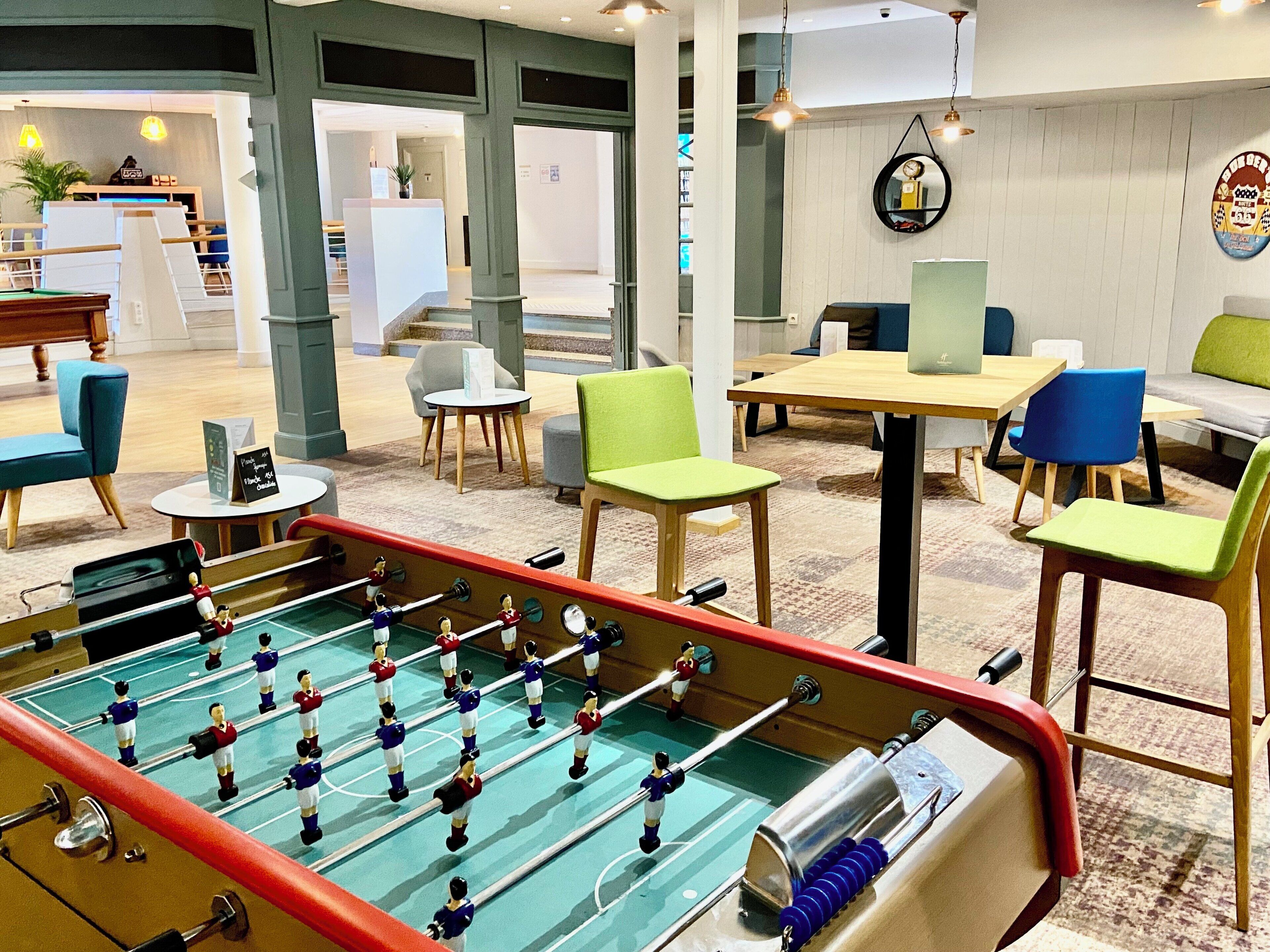A modern indoor space with a foosball table, seating areas, and a reception desk.
