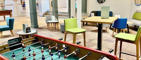A modern indoor space with a foosball table, seating areas, and a reception desk.