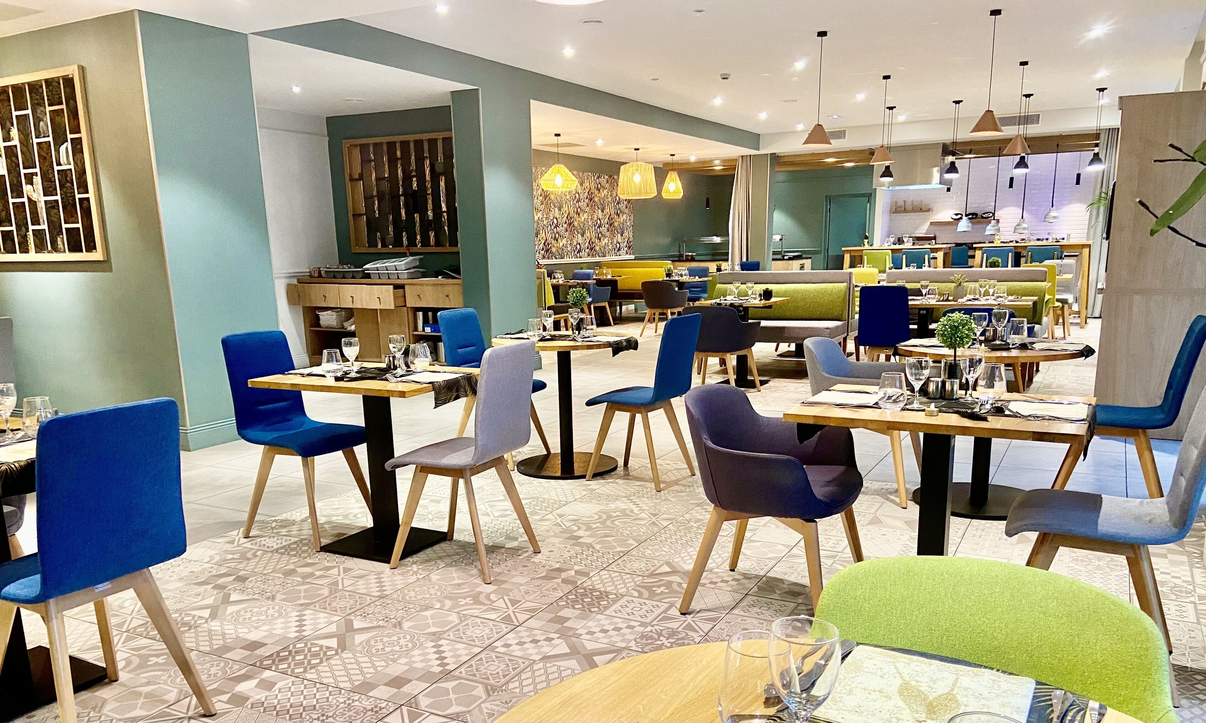 Un restaurante moderno con sillas azules y grises, mesas de madera y baldosas de suelo con diseños.