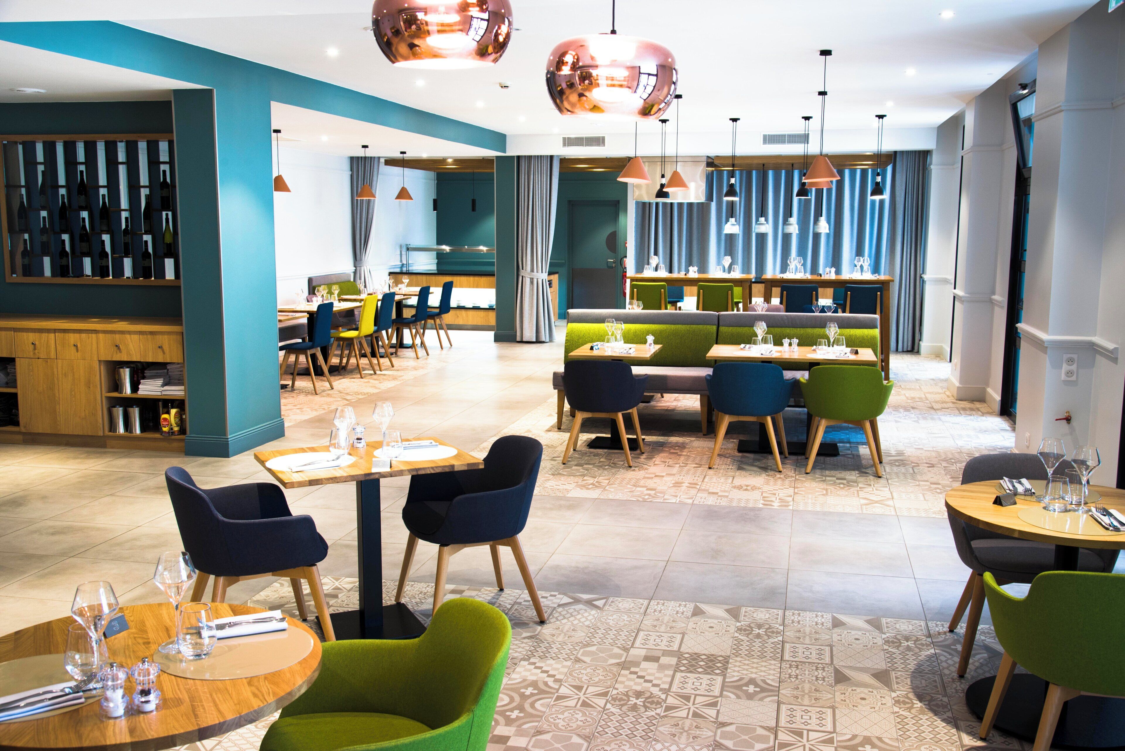Un interior de restaurante moderno con varias zonas de comedor, incluidas mesas y cabinas, y un área de bar con una exhibición de vinos.