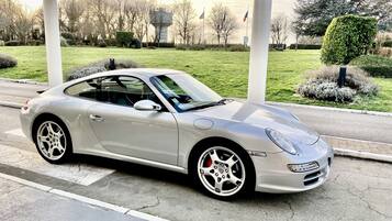 A silver sports car parked at a gas station with a grassy area and trees in the background.