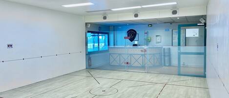 Ein Squashplatz mit Glasabtrennung, Deckenleuchten und einer Uhr an der Wand.