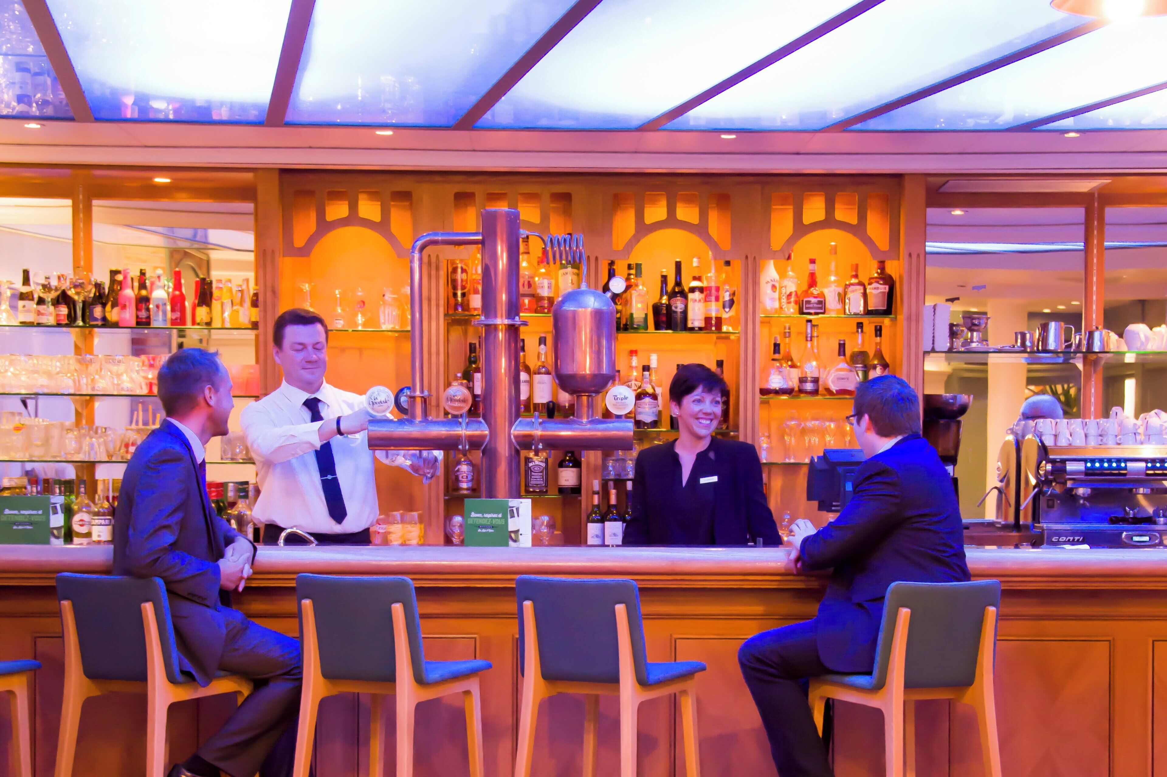 A bar area with multiple seating arrangements and a variety of bottles on shelves.