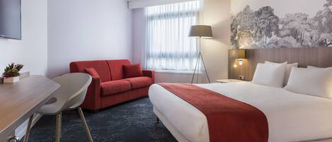 Una habitación de hotel con una cama, un sofá rojo, un escritorio y una lámpara.