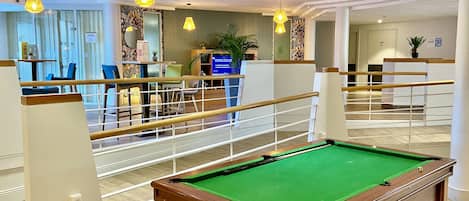 A pool table in a hotel lobby with a view of the reception area and a staircase.