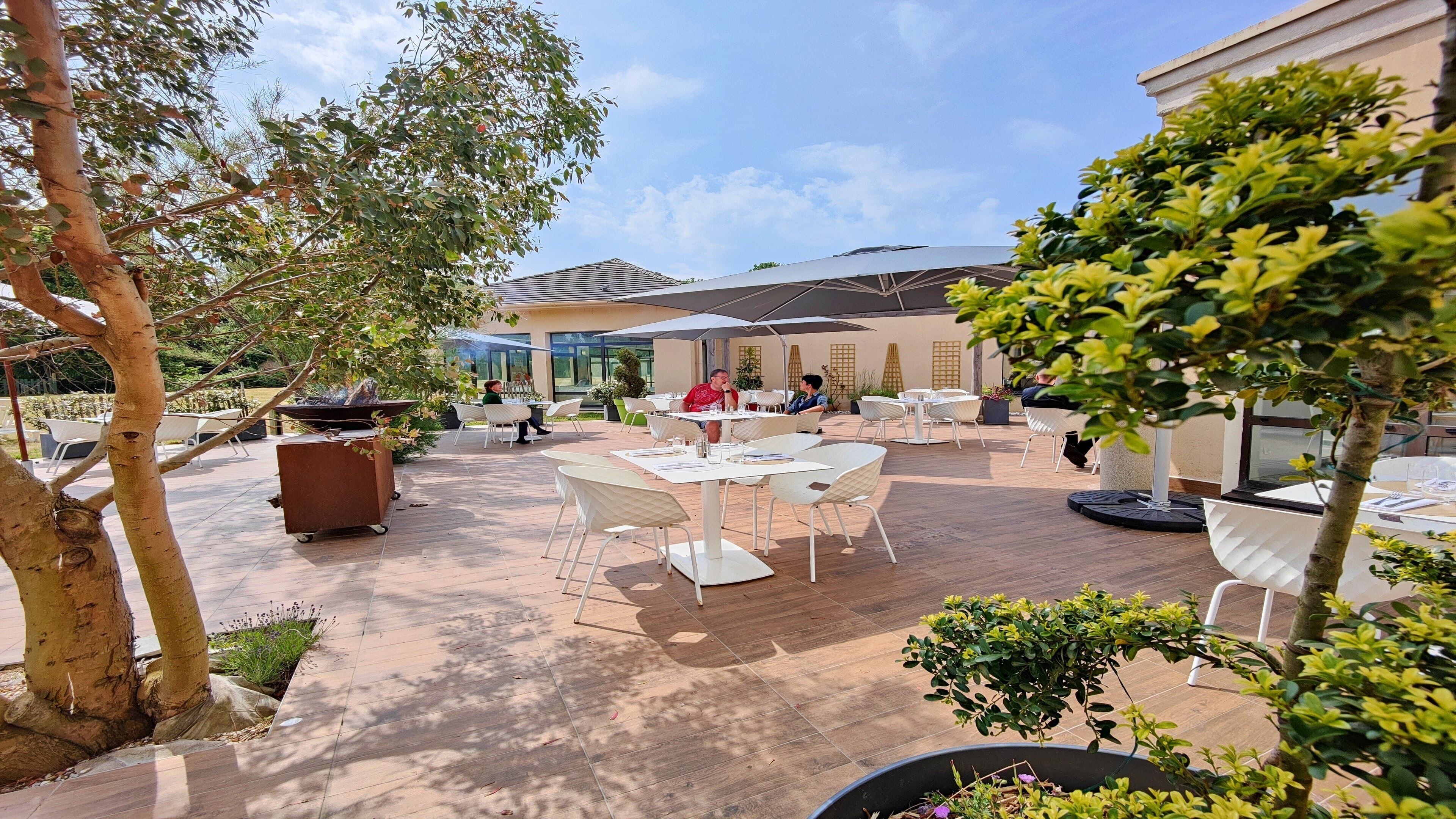 An outdoor patio area with tables and chairs, surrounded by trees and plants.