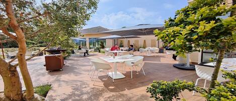 An outdoor patio area with tables and chairs, surrounded by trees and plants.
