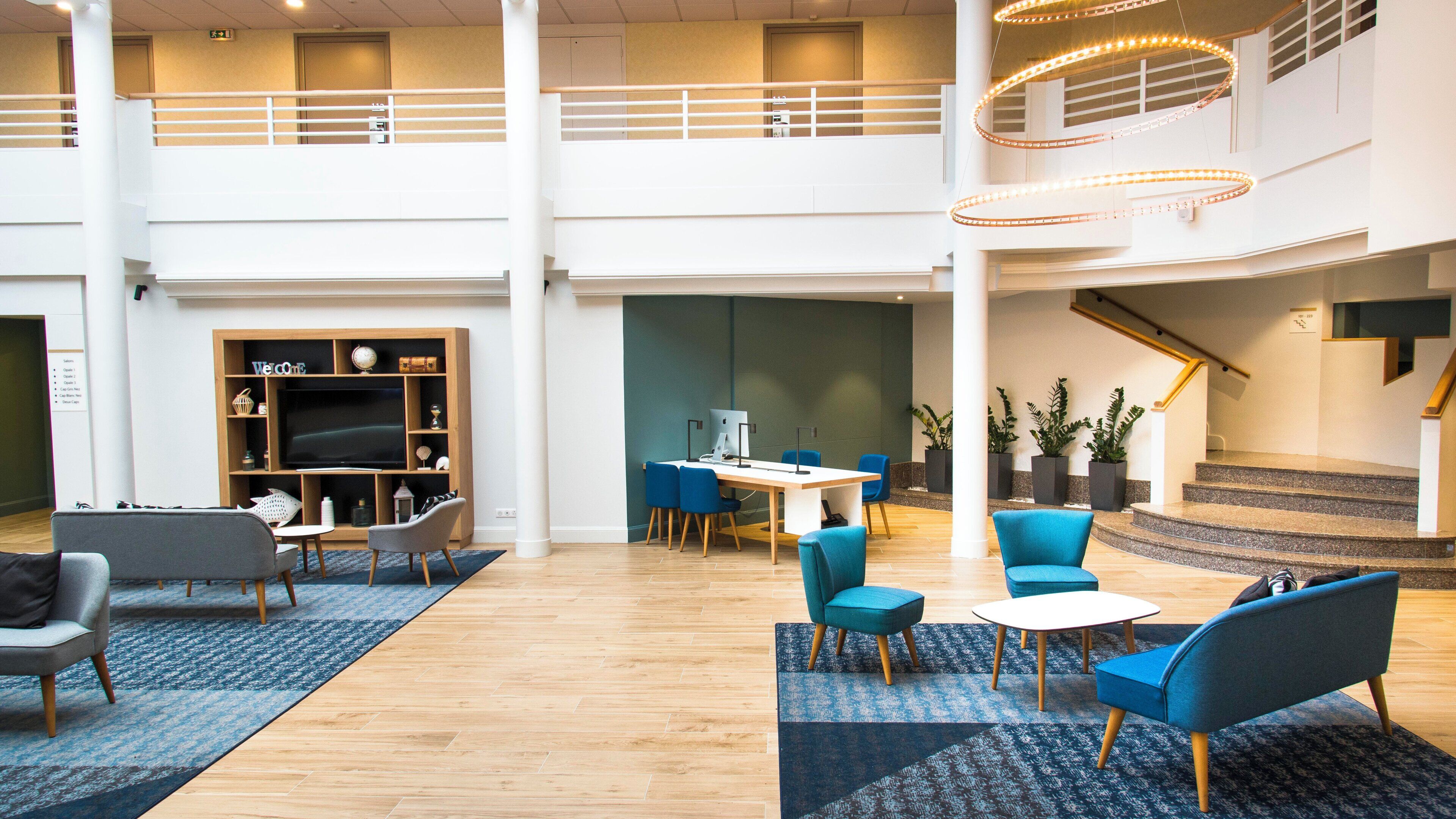 A spacious lobby with a high ceiling, a staircase, and a seating area with blue chairs and a wooden desk.