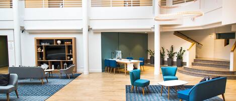 A spacious lobby with a high ceiling, a staircase, and a seating area with blue chairs and a wooden desk.