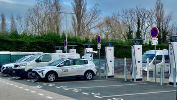 A parking area with electric vehicle charging stations, marked lanes, and a white car with 'TSG' branding.