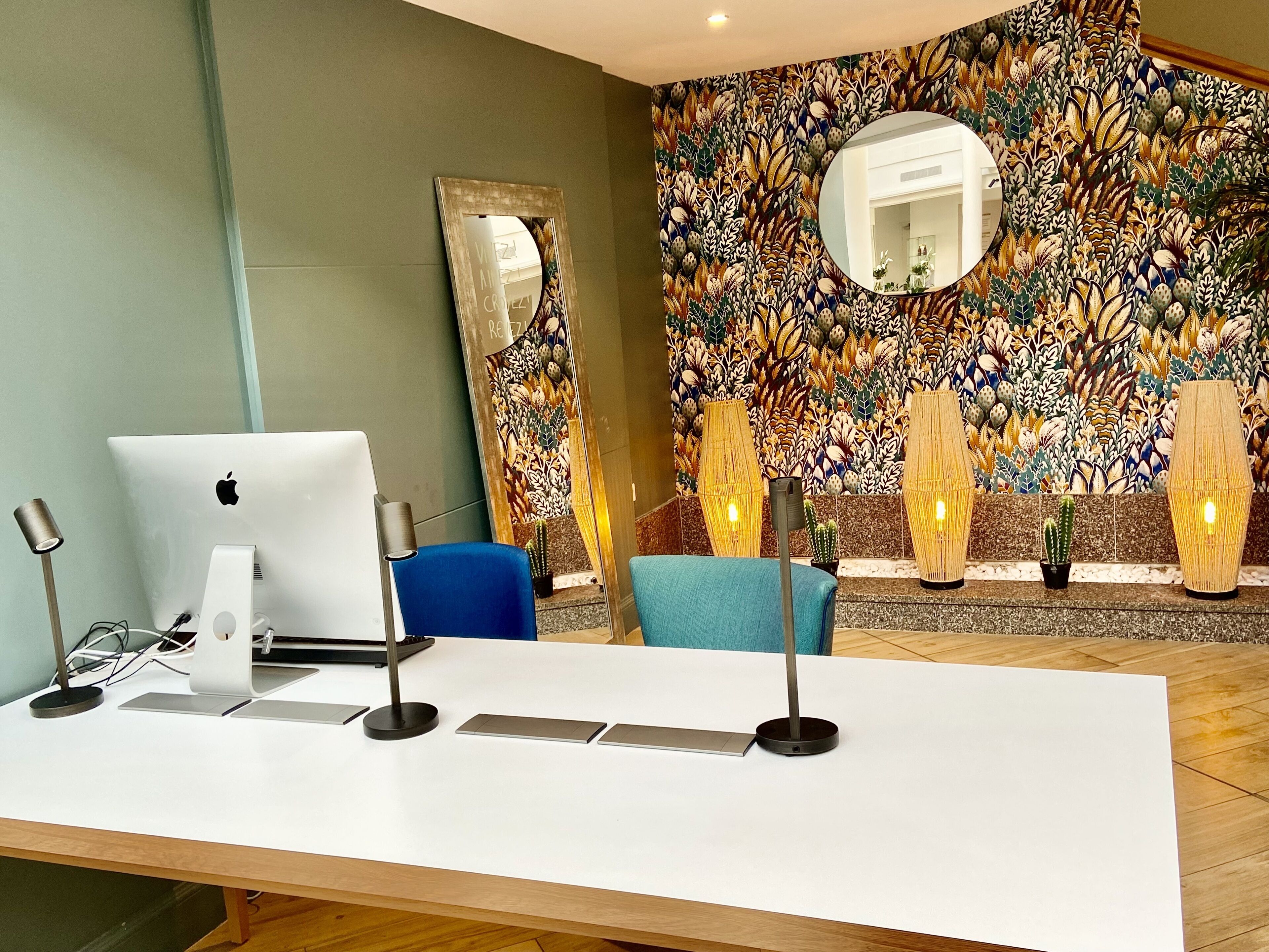 A reception desk with a laptop, a blue chair, and a decorative wall with a mirror and cacti.