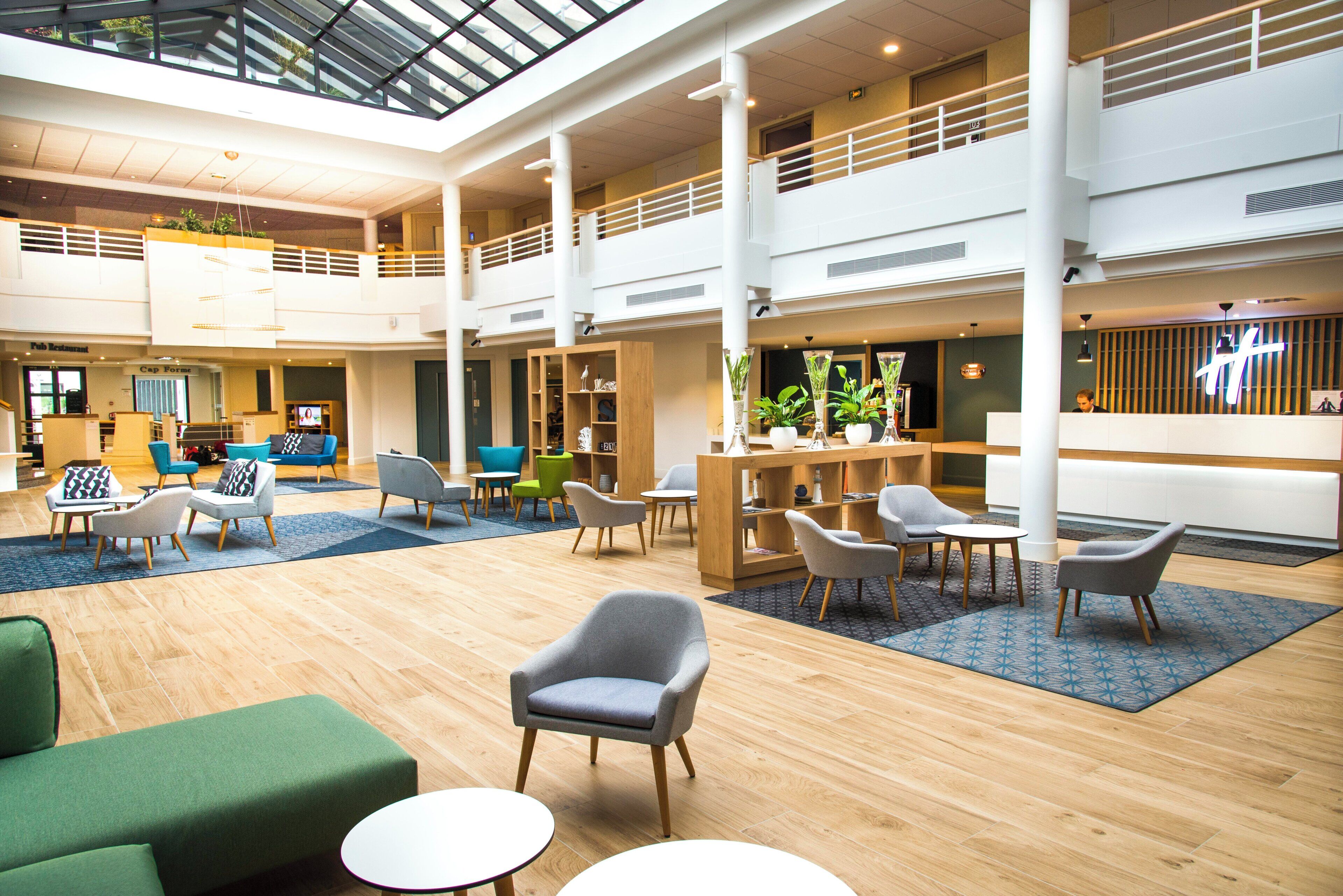 Een ruime lobby met diverse zithoeken, een receptiebalie en een hoog plafond met dakramen.
