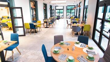 A modern dining area with multiple tables and chairs, large windows, and a clean, contemporary design.