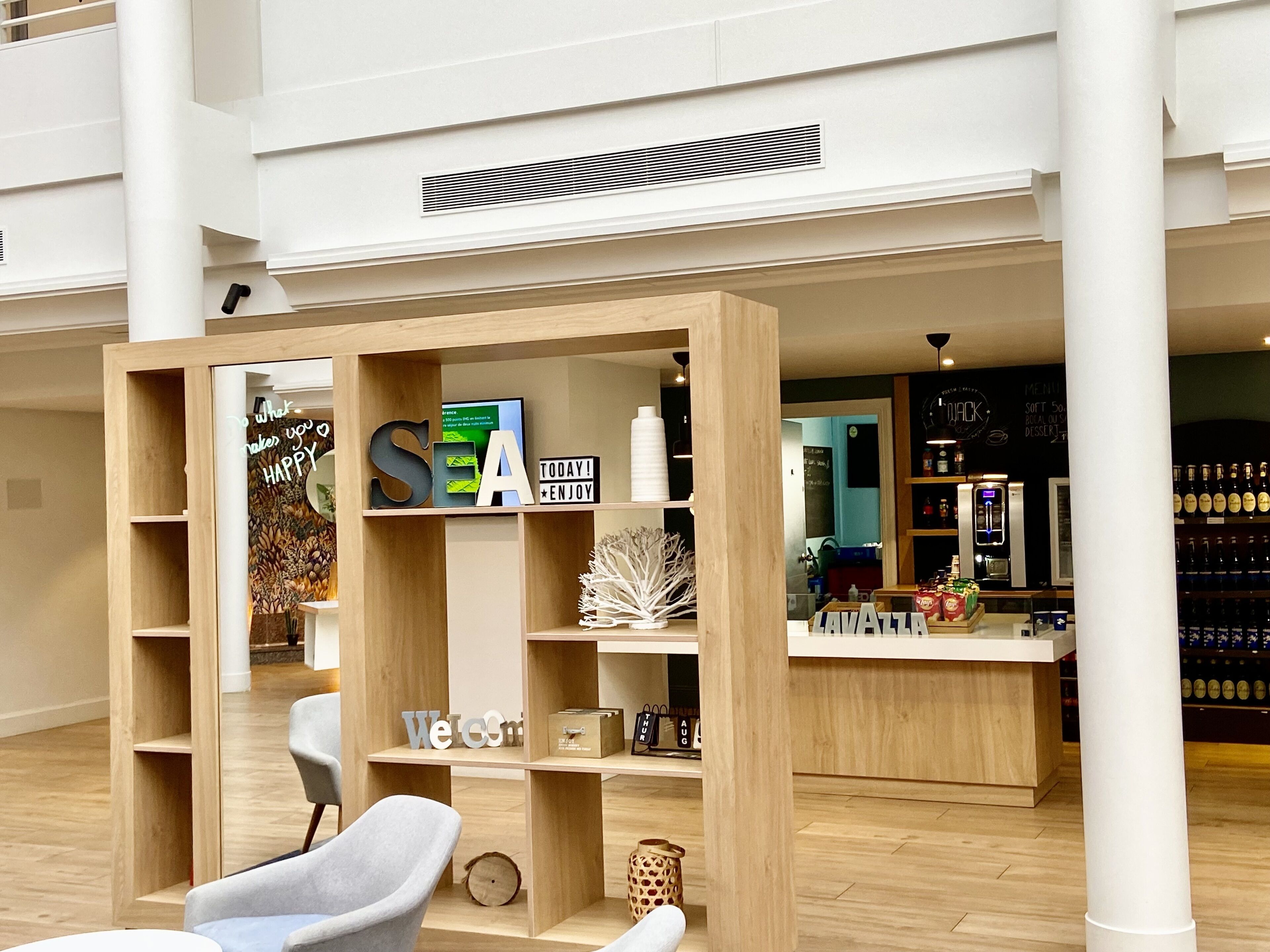 A modern interior with a wooden reception desk, a seating area with a grey chair, and a wall with a chalkboard menu.