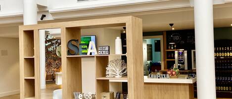 A modern interior with a wooden reception desk, a seating area with a grey chair, and a wall with a chalkboard menu.