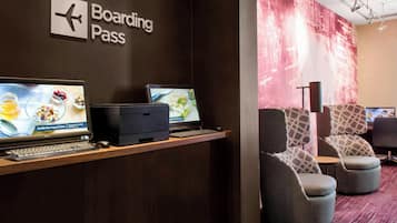A boarding pass station with two computer monitors, a keyboard, and a printer. There are two upholstered chairs and a small table.
