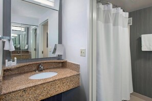 A bathroom with a granite countertop sink, a mirror, and a shower curtain.