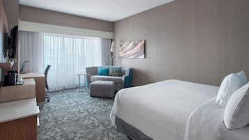 Habitación de hotel con una cama grande, un escritorio con computadora, una silla y un sofá con cojines.