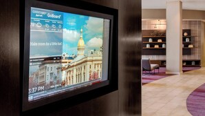 A hotel room with a large digital display showing the weather and a view of a historic building. - Courtyard by Marriott Newark Elizabeth (Elizabeth)