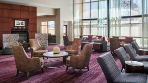 A spacious lobby with multiple seating areas, including sofas and armchairs, arranged around a central coffee table. Large windows provide ample natural light and a view of the outside. - Courtyard by Marriott Newark Elizabeth (Elizabeth)