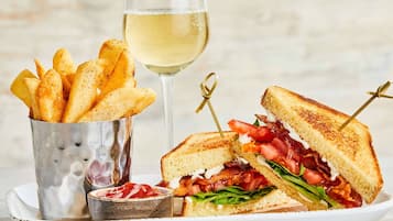 A sandwich with a toasted exterior, accompanied by a glass of white wine and a container of seasoned fries.