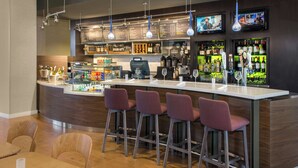 A bar area with a counter, bar stools, a cash register, and a menu board. - Courtyard by Marriott Newark Elizabeth (Elizabeth)